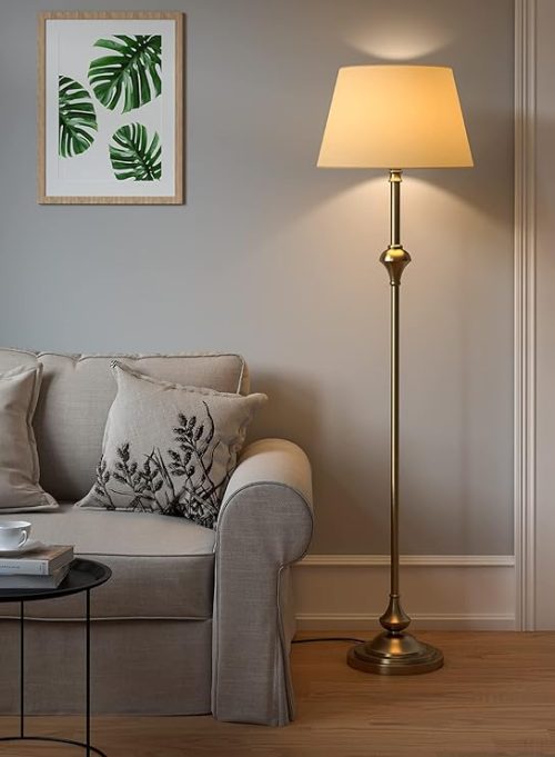 Elegant brass antique finish LED floor lamp with cream lampshade standing beside a sofa in a modern living room