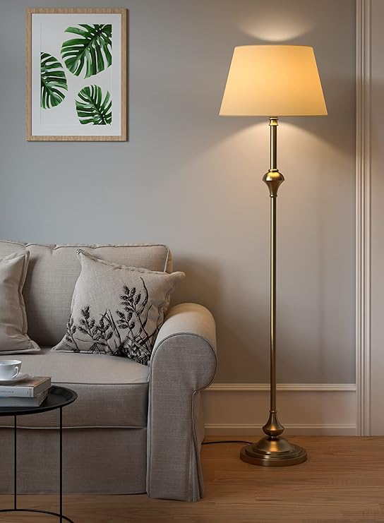 Elegant brass antique finish LED floor lamp with cream lampshade standing beside a sofa in a modern living room