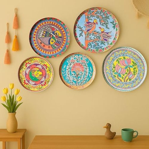 Colorful metal wall decor items – set of five Madhubani plates displayed on a beige wall above a wooden table.