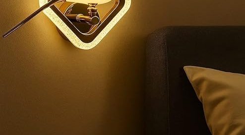 A decorative Bedroom Lamp Wall sconce shaped like a glowing gold bird in a square frame, casting warm light above a nightstand.