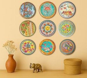 A set of nine circular, decorative plates on a wall, showcasing a creative style of wall decor hanging with colorful folk art designs.